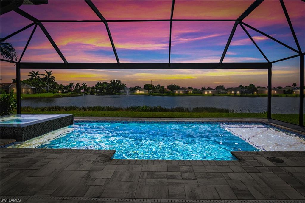 Pool at dusk with a water view, a lanai, and an in ground hot tub