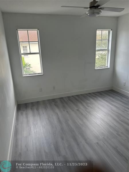 an empty room with wooden floor windows and fan