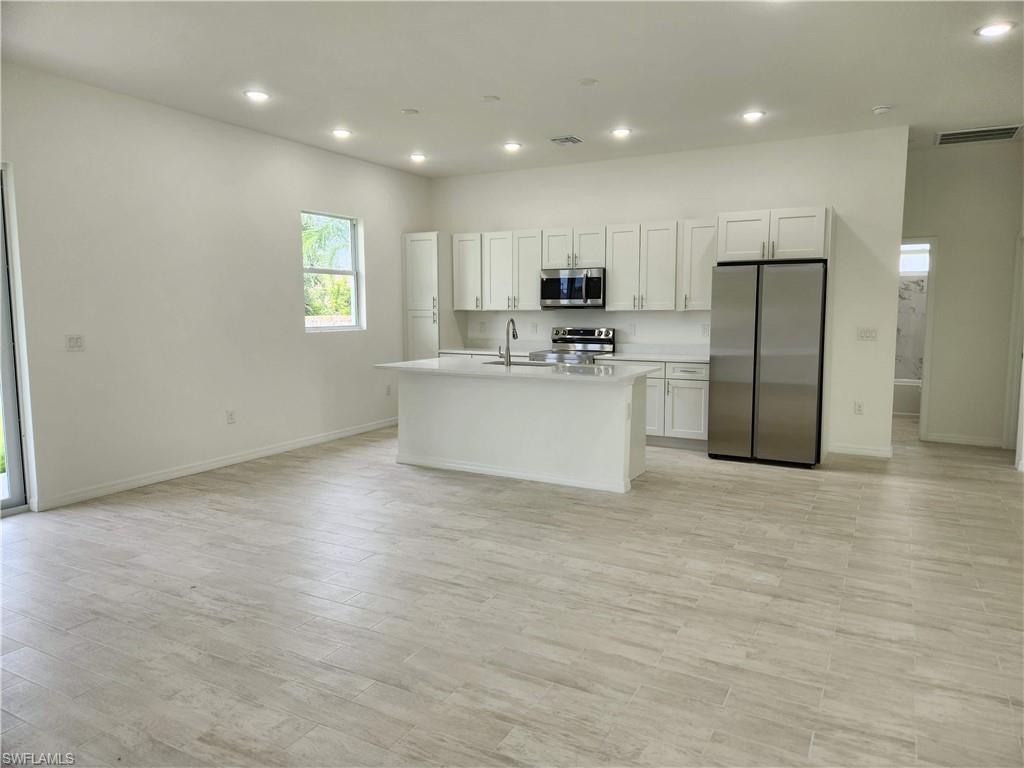 a view of kitchen with kitchen island stainless steel appliances cabinets a sink and a window