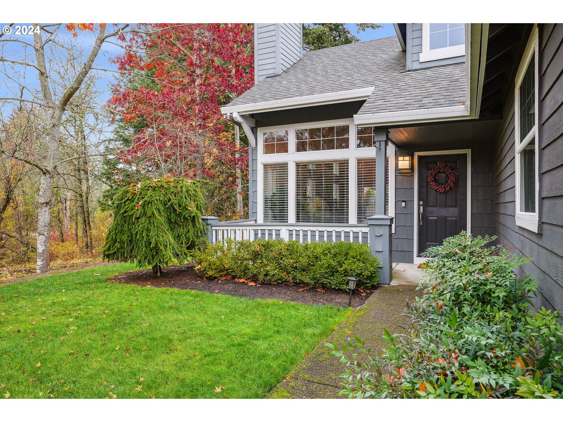 a view of a brick house with a yard plants and a large tree