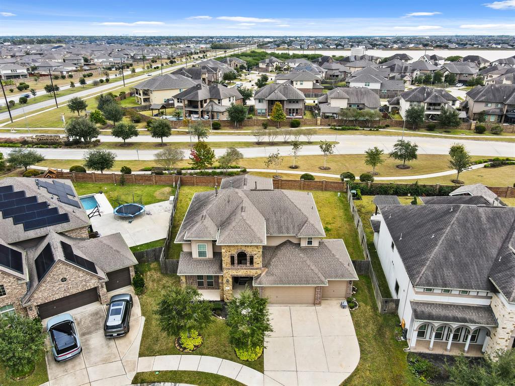 This aerial view showcases a spacious two-story home with a large driveway and manicured lawn, nestled in a well-maintained suburban neighborhood. The property features a fenced backyard and is surrounded by other modern homes, offering a sense of community and convenience.