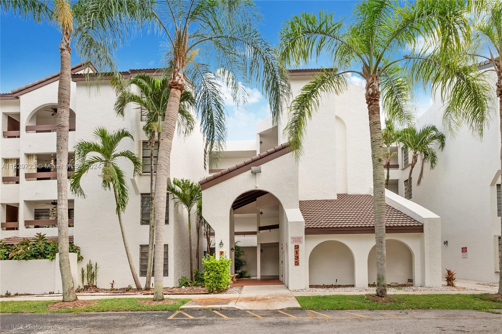 a view of a white house with a palm trees and a small yard