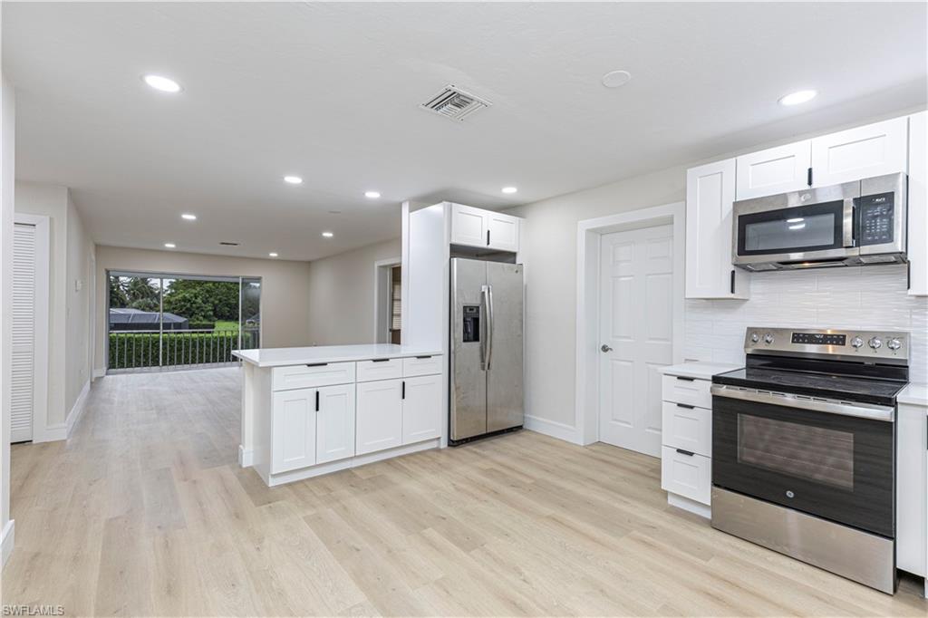 Kitchen with white cabinetry, light wood-type flooring, stainless steel appliances, and kitchen peninsula