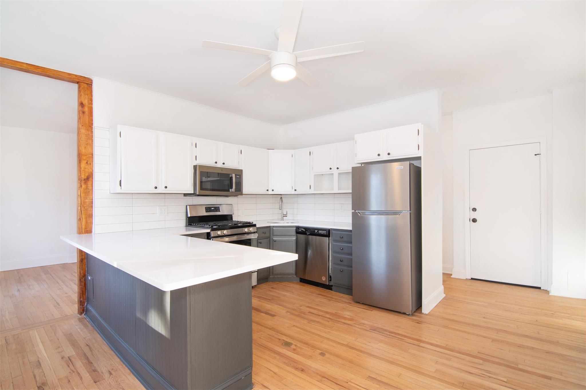 Kitchen with light hardwood flooring, backsplash, kitchen peninsula, white cabinets, and appliances with stainless steel finishes