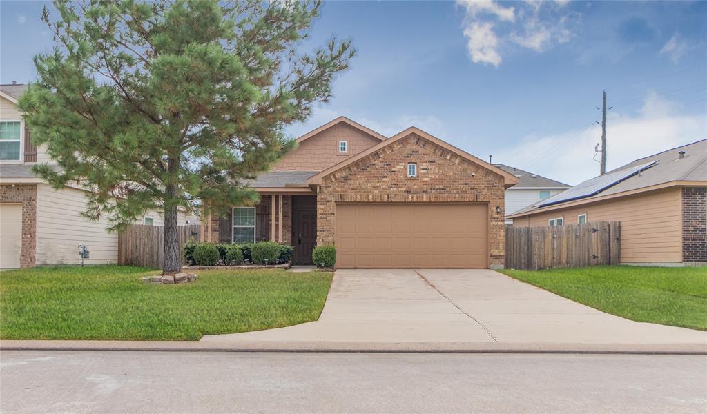 This is a single-story brick home featuring a two-car garage, a well-maintained lawn, and a mature tree in the front yard, providing both curb appeal and shade.