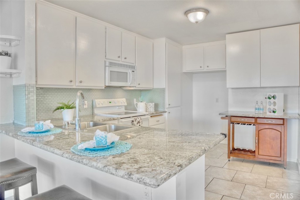 a kitchen with granite countertop a sink a stove and white cabinets