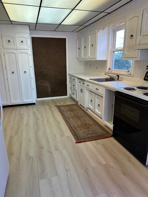 Kitchen with light wood-type flooring, tasteful backsplash, sink, electric range, and white cabinets