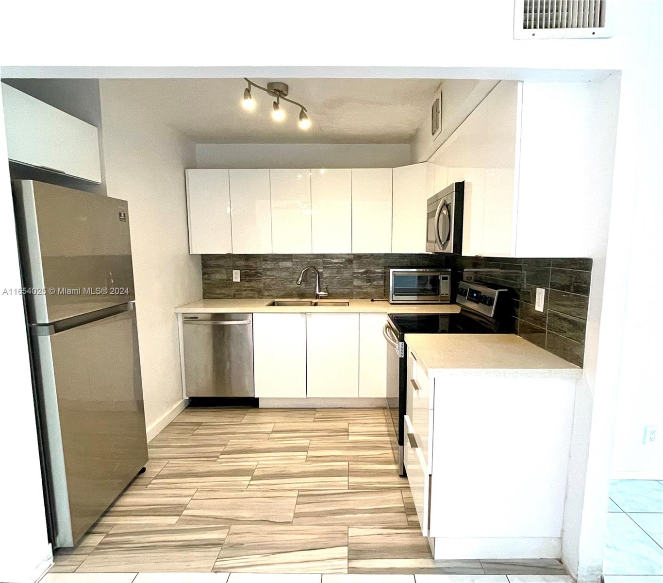 a kitchen with stainless steel appliances granite countertop a refrigerator a sink and white cabinets