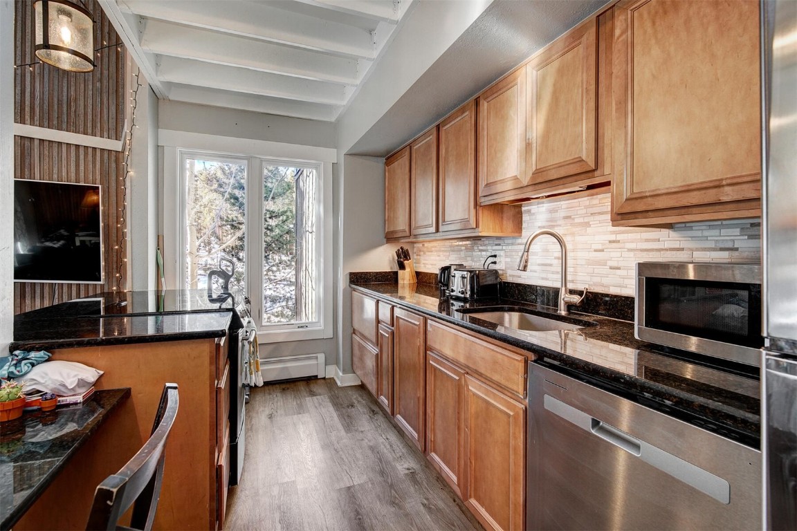 Kitchen featuring a stone fireplace, sink, stainless steel dishwasher, dark stone countertops, and beam ceiling