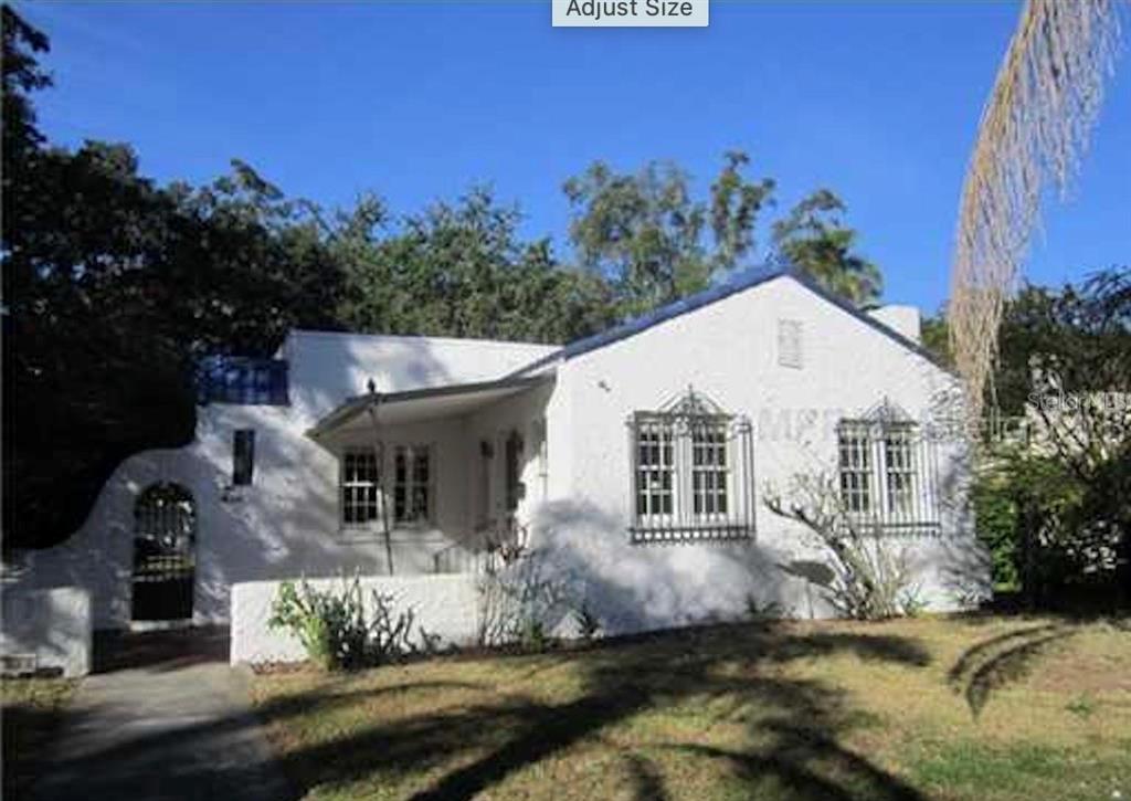 a view of a white house with a small yard plants and large tree