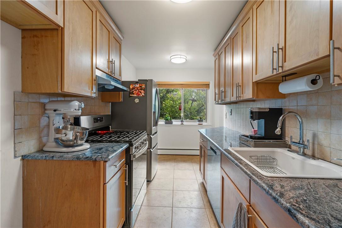 Kitchen with tasteful backsplash, stainless steel appliances, sink, dark stone counters, and light tile patterned flooring