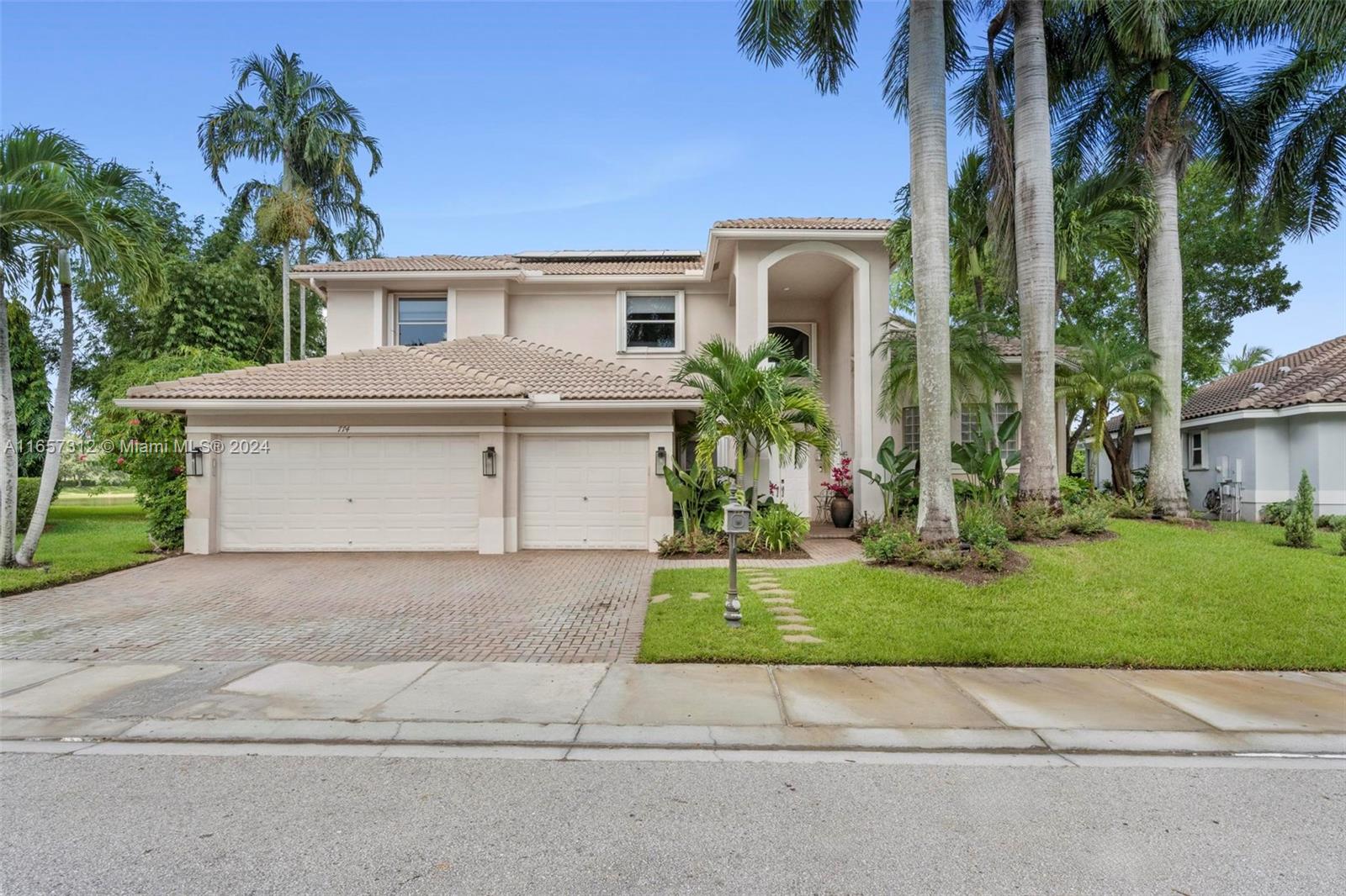 a view of a white house with a large windows and a yard with palm trees