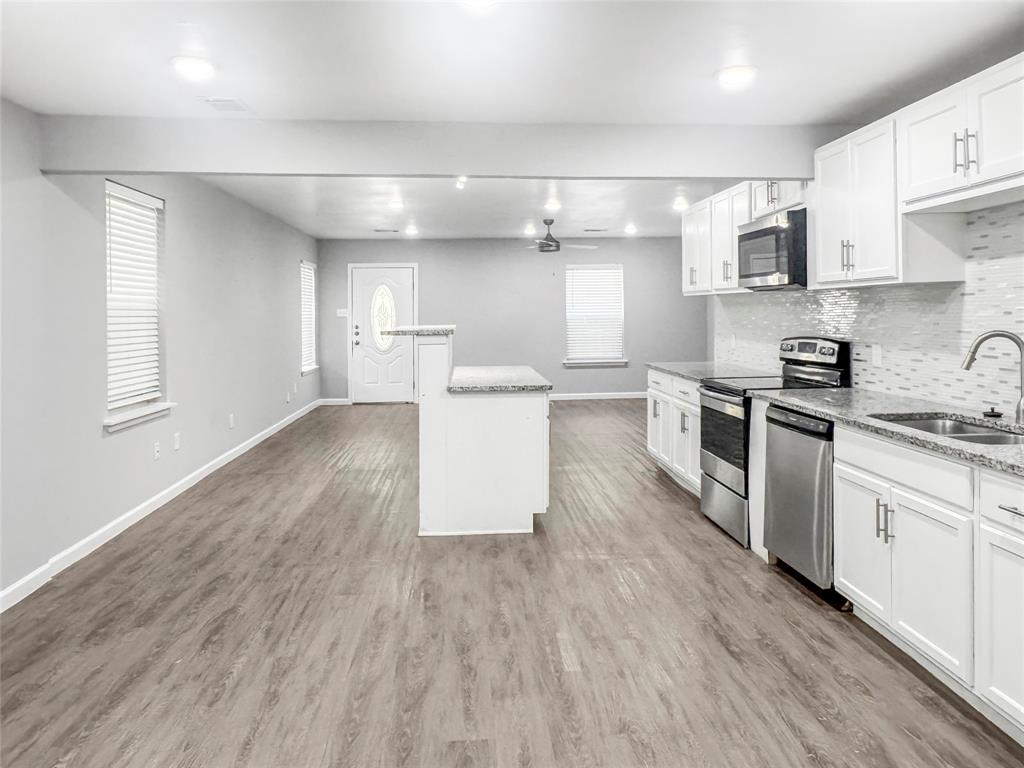 Kitchen with white cabinetry, stainless steel appliances, sink, and light stone counters