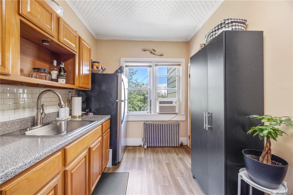 Kitchen with light wood-type flooring, ornamental molding, backsplash, sink, and radiator