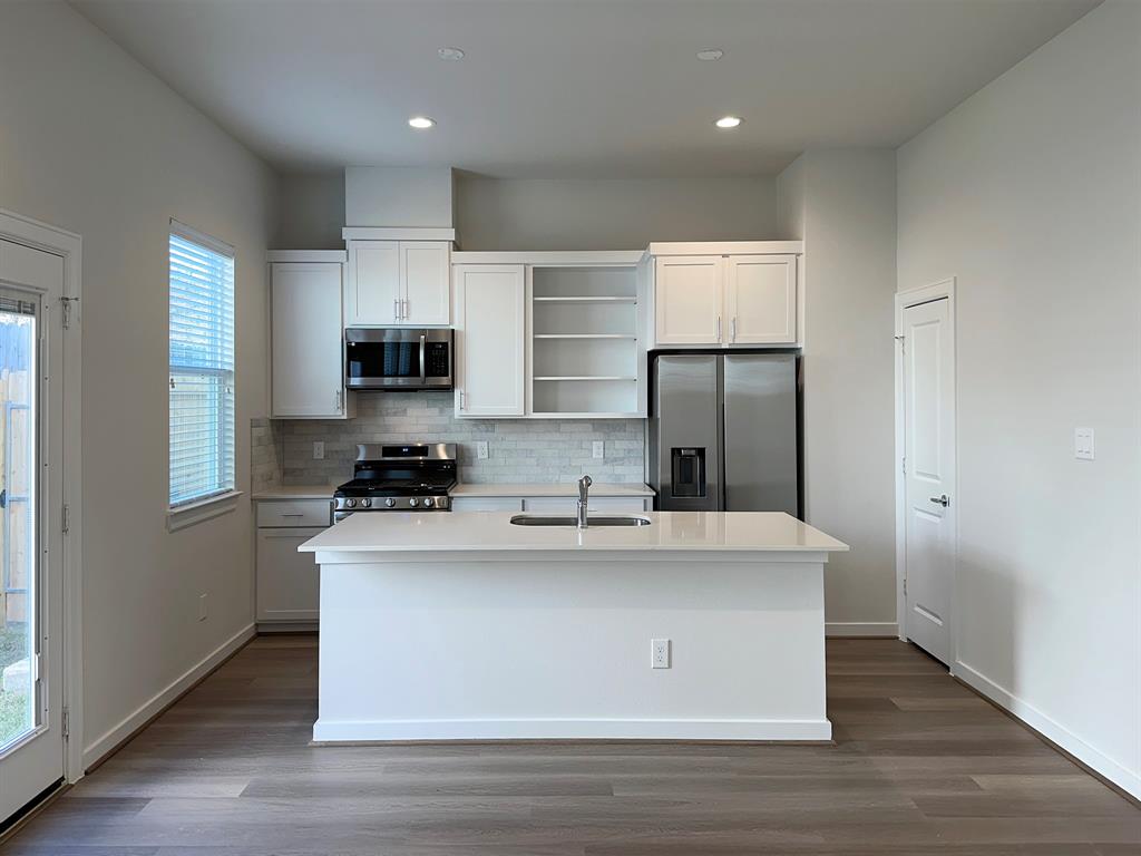 a view of a kitchen with kitchen island a sink wooden floor and stainless steel appliances