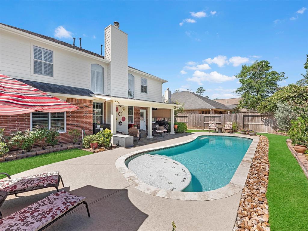 This is a spacious backyard featuring an inviting swimming pool with an integrated hot tub, a well-maintained lawn, and a cozy covered patio area, all complementing a two-story brick home with ample outdoor space for relaxation and entertainment.