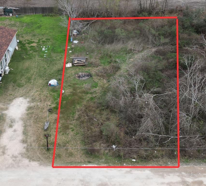 This photo shows a rectangular double lot plot of land, partially cleared with some grass and brush. The area is outlined in red for clarity.