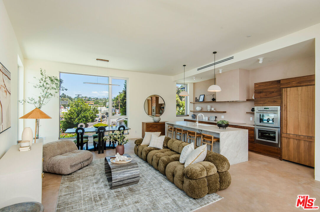 a living room with stainless steel appliances furniture a rug and a large window