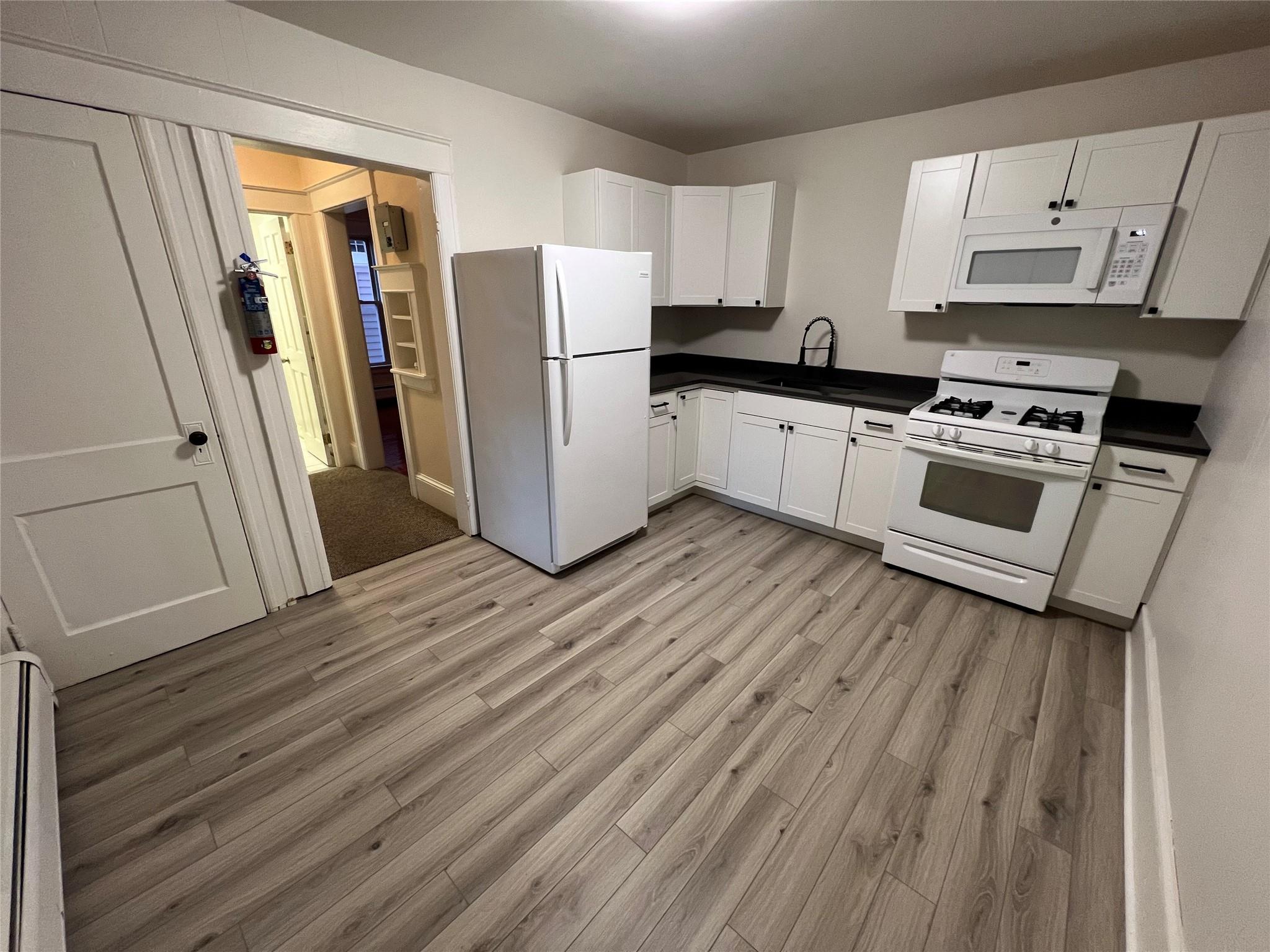 Kitchen featuring white cabinets, light wood-type flooring, white appliances, and sink