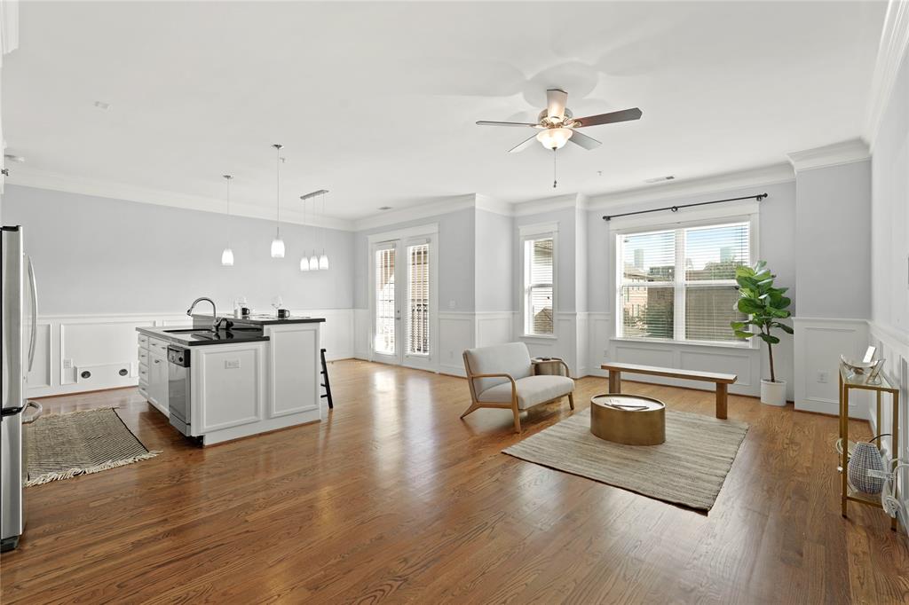 Bright, open-concept living space with a combined kitchen and living area. It features hardwood floors, white cabinetry, stainless steel appliances, and ample natural light from large windows and French doors leading to a lovely balcony.