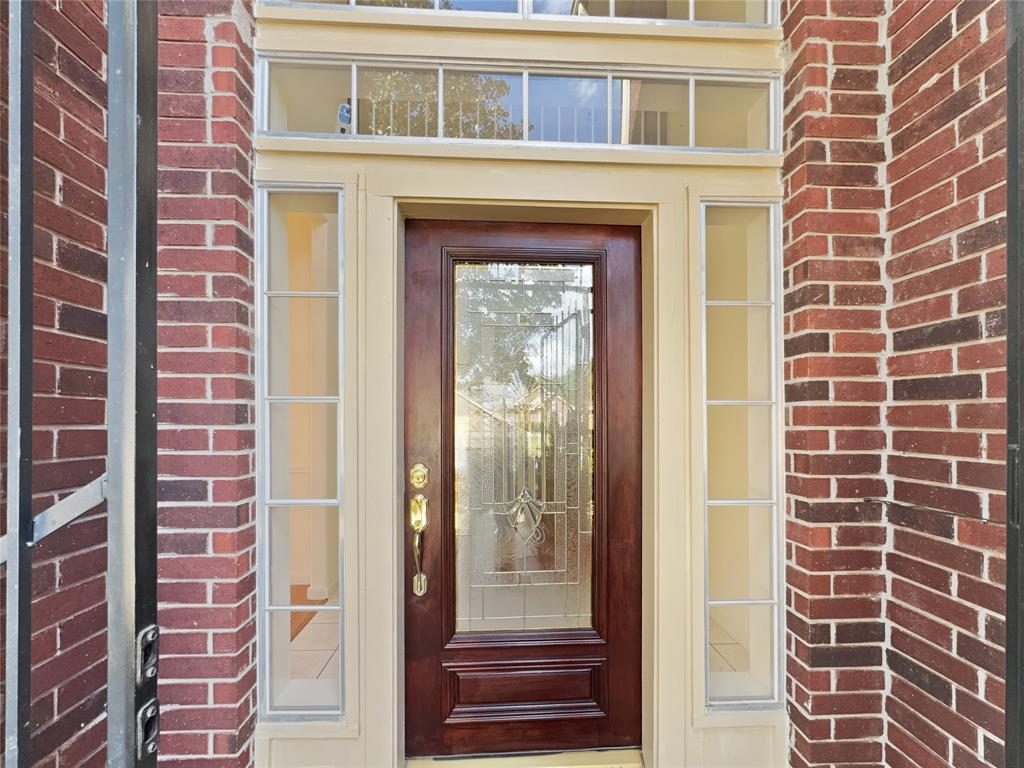 This is an elegant front door framed by cream-colored trim and red brickwork, featuring a large wood door with glass insert and sidelights, providing a welcoming entrance to the home.