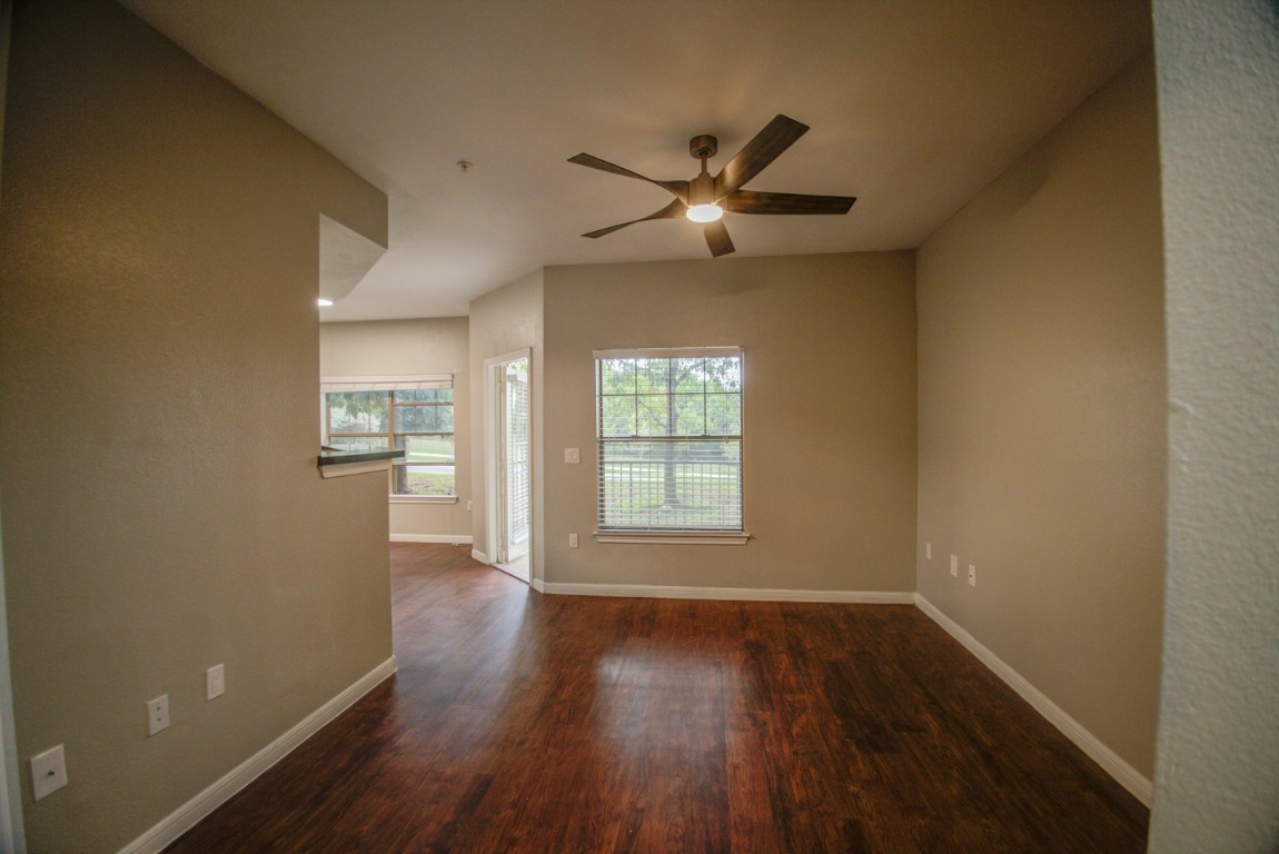 an empty room with wooden floor a ceiling fan and windows