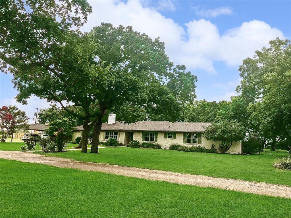 a view of house in front of a big yard with large trees