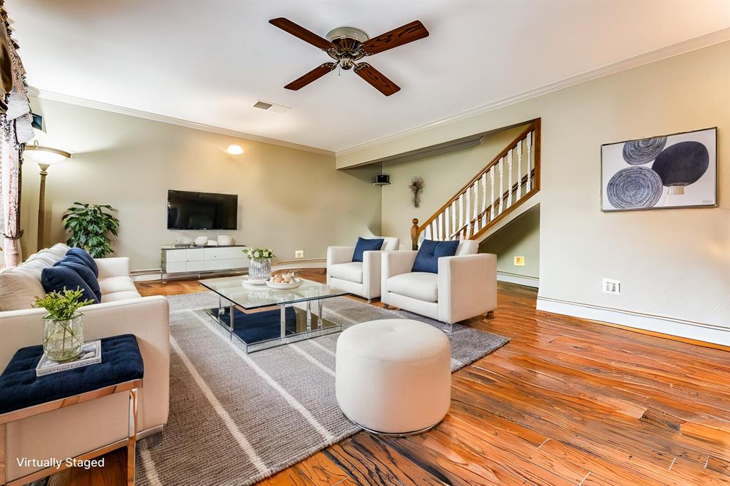 a living room with couches a flat screen tv and kitchen view with wooden floor