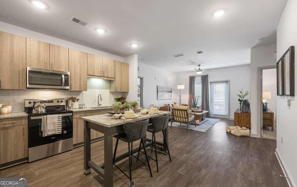 a kitchen with stainless steel appliances kitchen island granite countertop a stove top oven a sink dishwasher a dining table and chairs with wooden floor