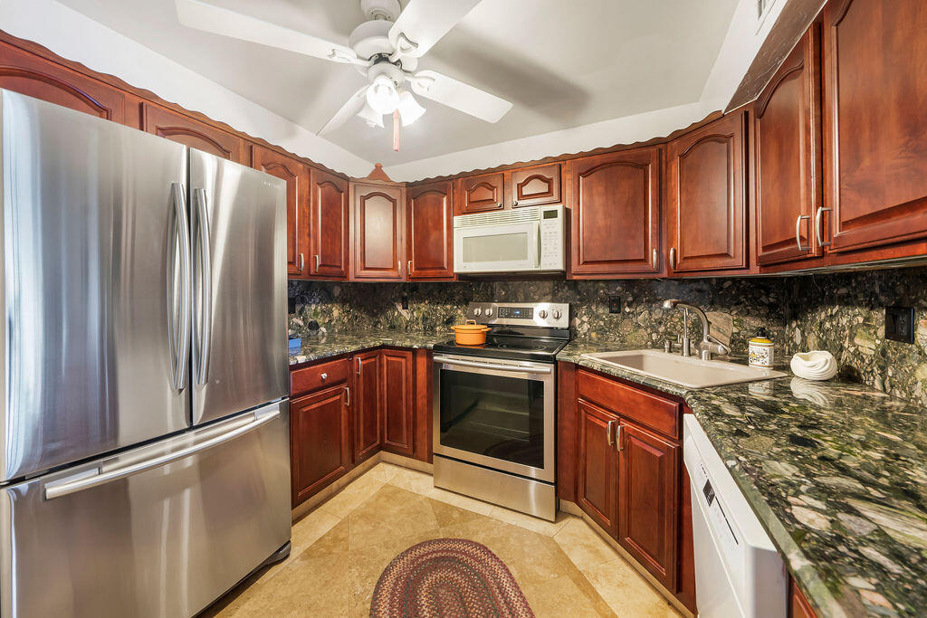 a kitchen with stainless steel appliances granite countertop a refrigerator a stove and a sink with wooden cabinets