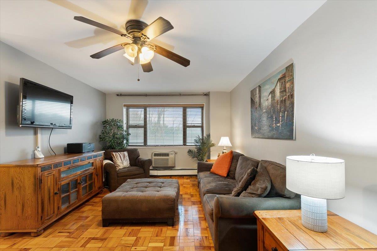 Living room with a wall mounted air conditioner, ceiling fan, and light parquet floors