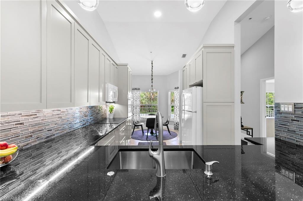 Kitchen with white appliances, tasteful backsplash, decorative light fixtures, white cabinets, and dark stone countertops