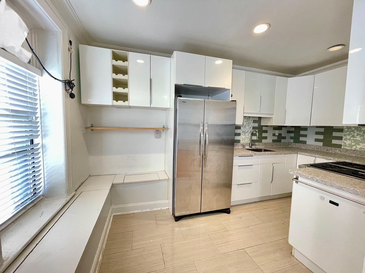 Kitchen with decorative backsplash, white cabinetry, stainless steel refrigerator, and sink