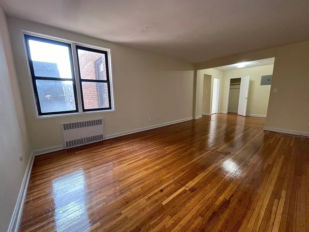 a view of an empty room with wooden floor and a window