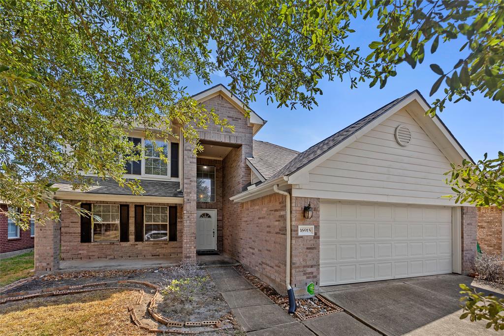 This is a two-story, brick-facade home featuring a two-car garage and mature trees on the front lawn, situated in a well-maintained suburban neighborhood.