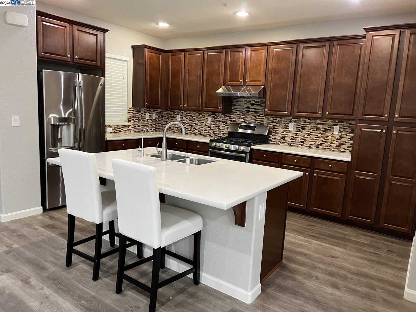 a kitchen with stainless steel appliances granite countertop a table chairs refrigerator and sink