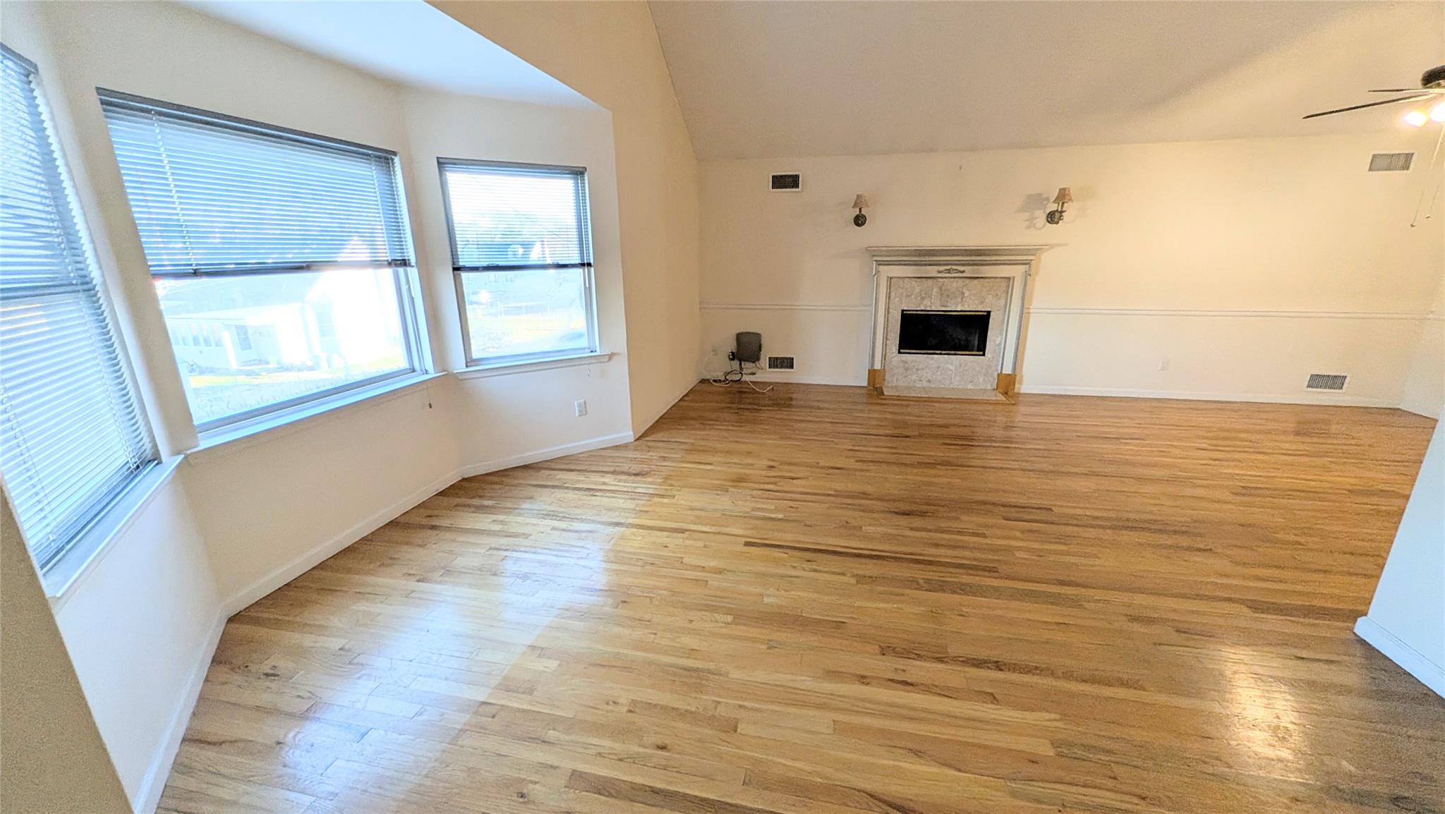 Unfurnished living room with a fireplace, light wood-type flooring, vaulted ceiling, and ceiling fan