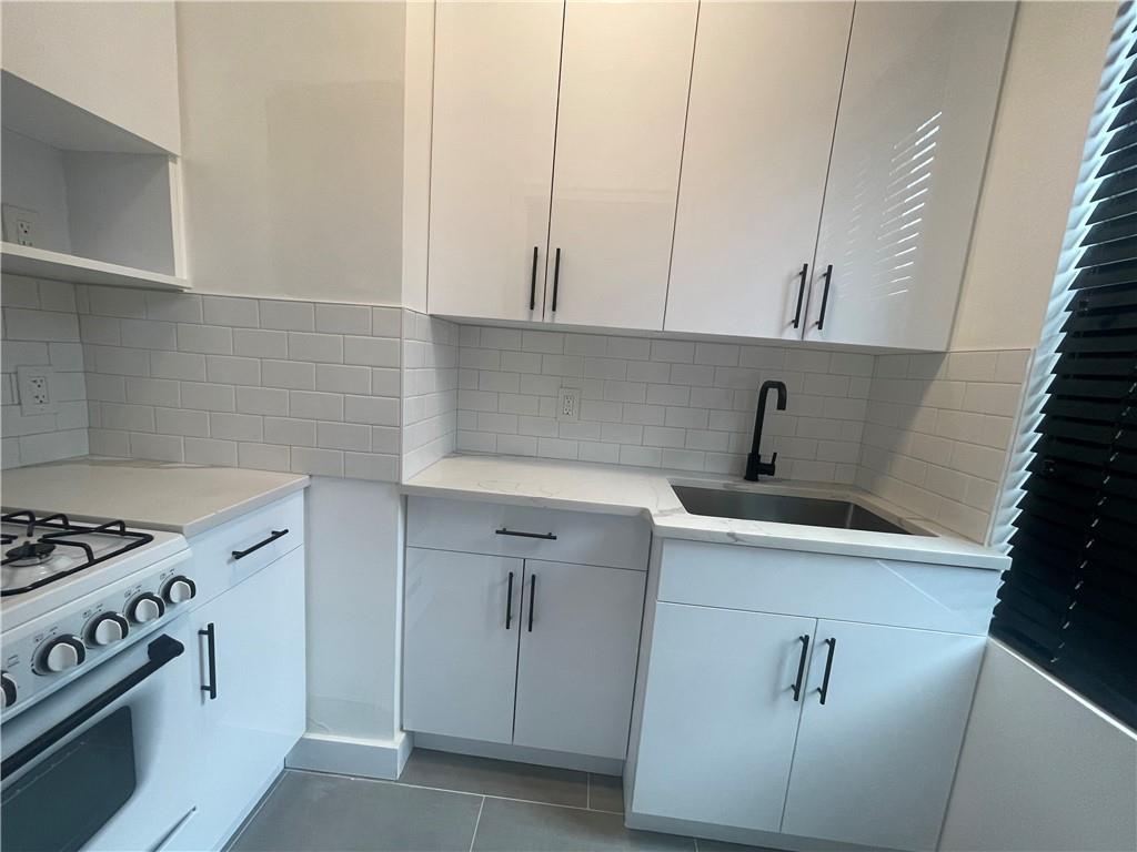 Kitchen with tasteful backsplash, white cabinetry, and sink