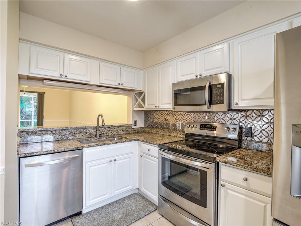 Kitchen with sink, dark stone countertops, decorative backsplash, white cabinets, and appliances with stainless steel finishes