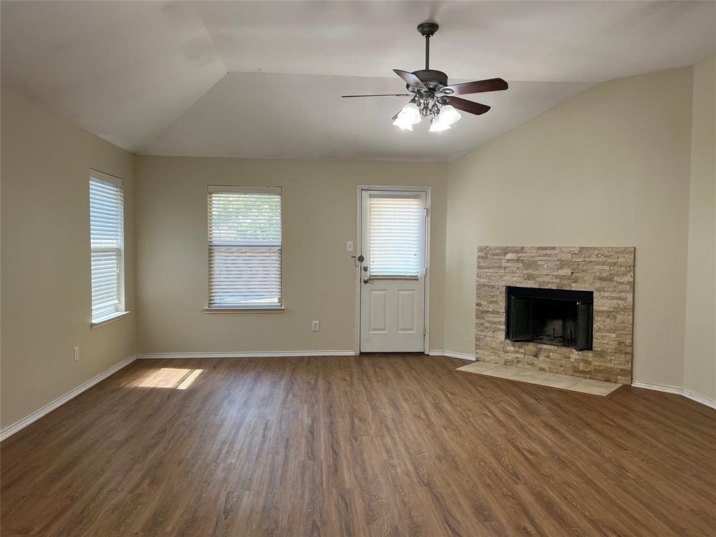 a view of an empty room with wooden floor fireplace and a window