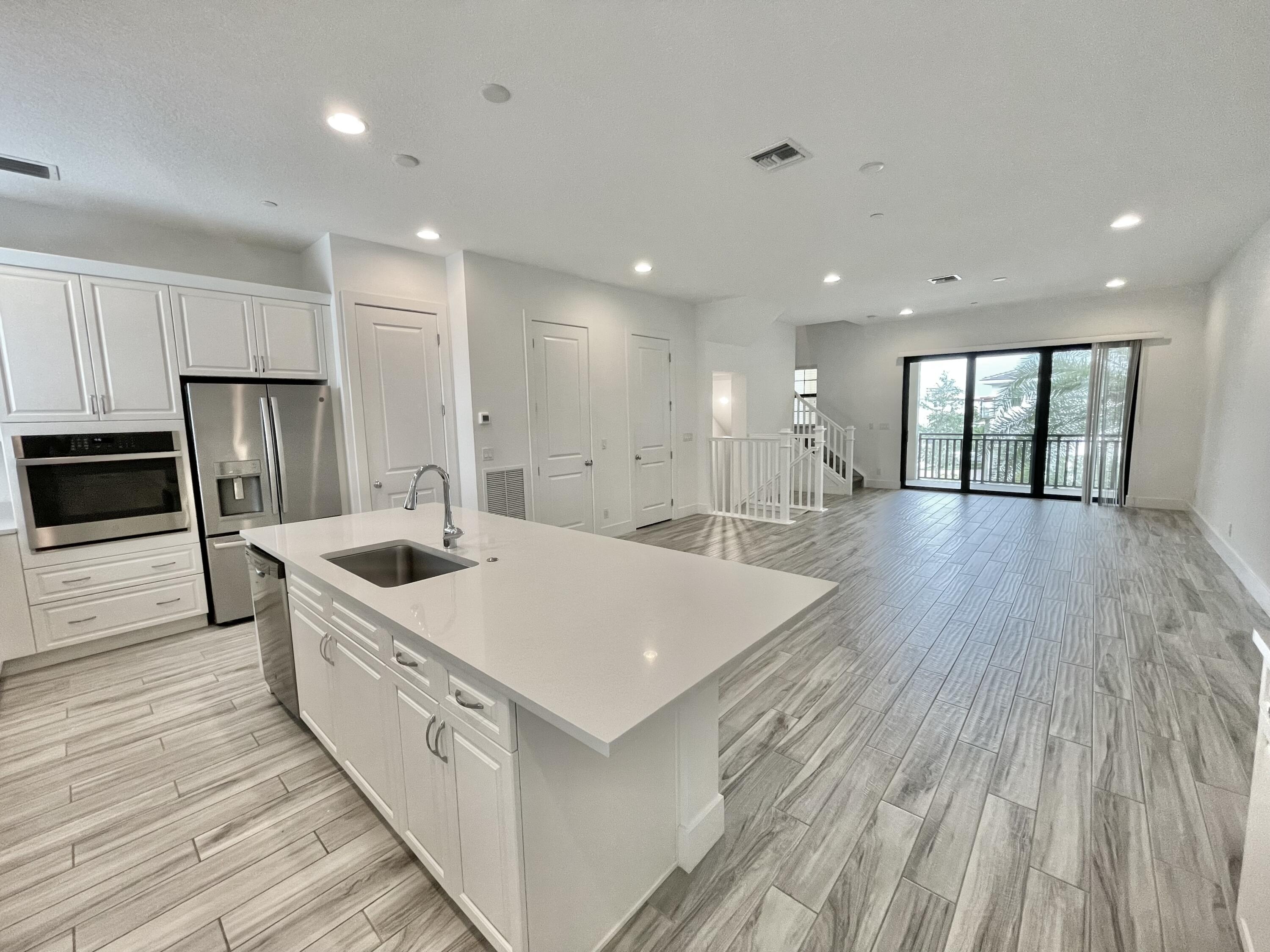 a large white kitchen with a sink a refrigerator and wooden floor