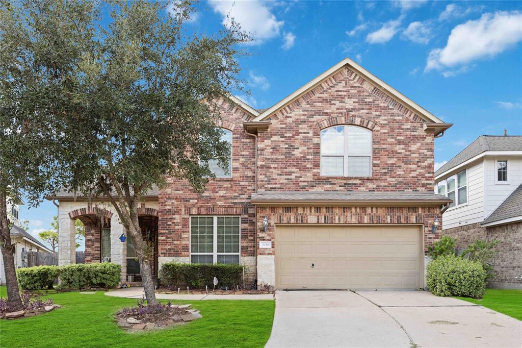 This is a two-story brick home featuring a landscaped front yard, an arched entryway, and a two-car garage, set in a residential neighborhood.