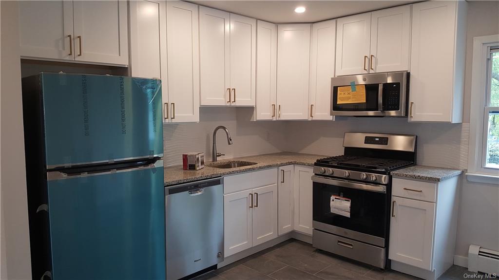 Kitchen with light stone countertops, a baseboard radiator, white cabinetry, and stainless steel appliances