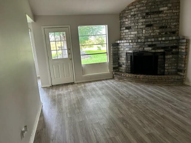 an empty room with wooden floor fireplace and windows