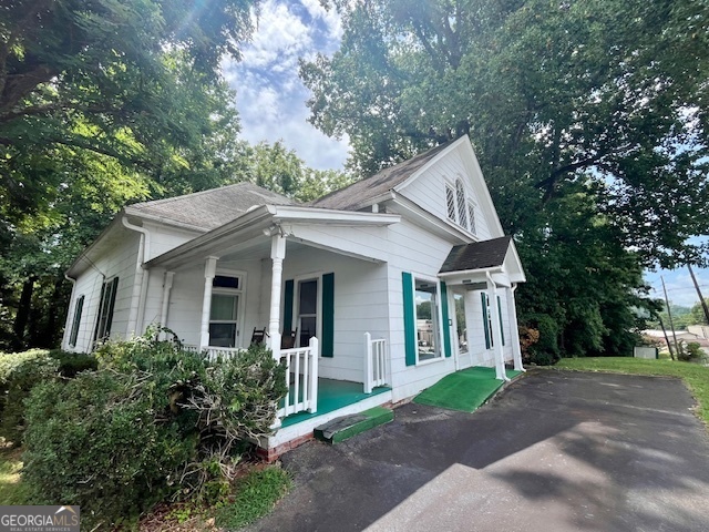 a view of a white house next to a yard with big trees