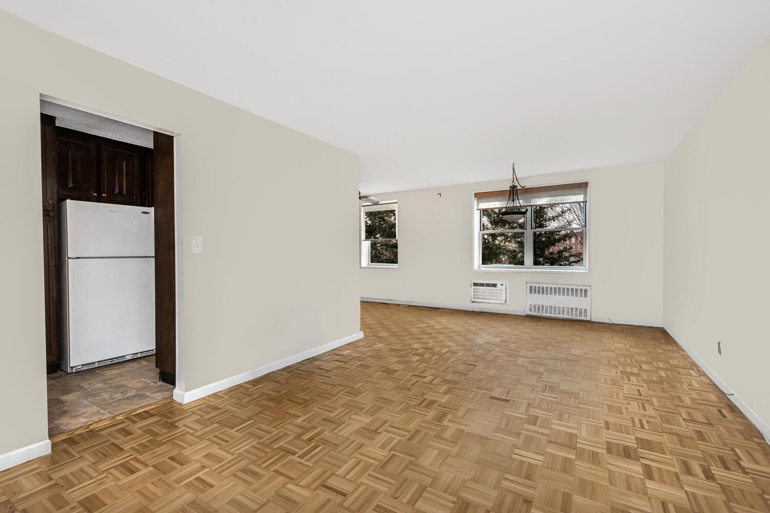 Unfurnished living room with radiator heating unit, light parquet floors, and a wall mounted air conditioner