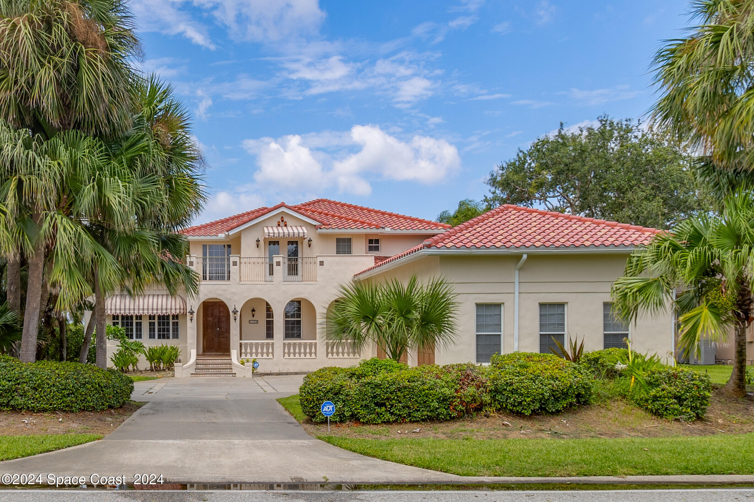 a view of a white house with a big yard and potted plants and palm trees