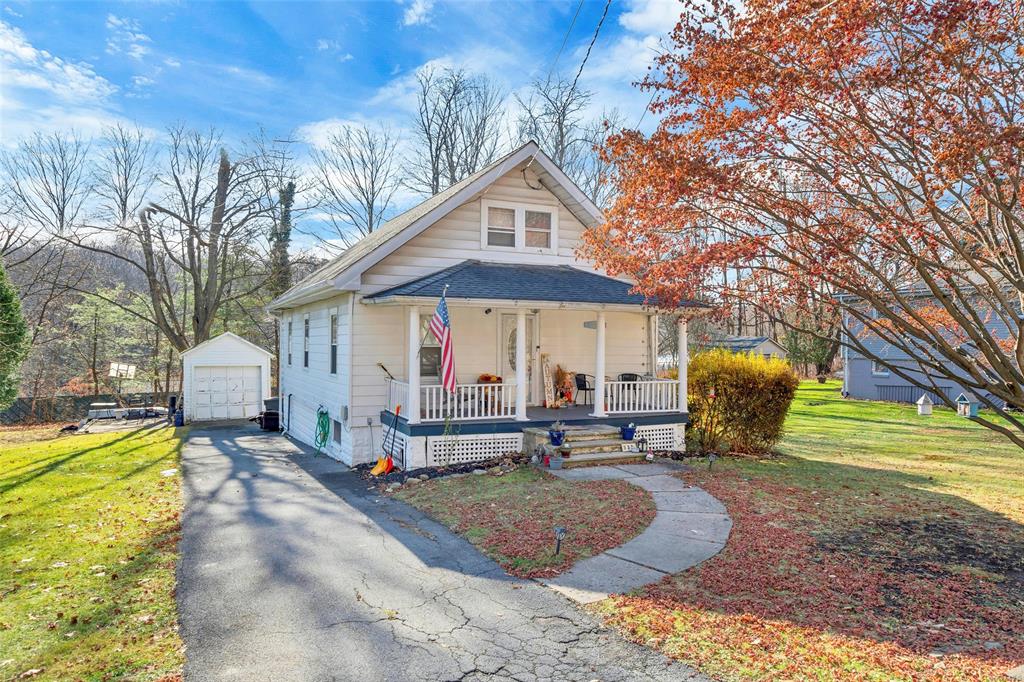 Home with a porch, a garage, an outbuilding, and a front yard