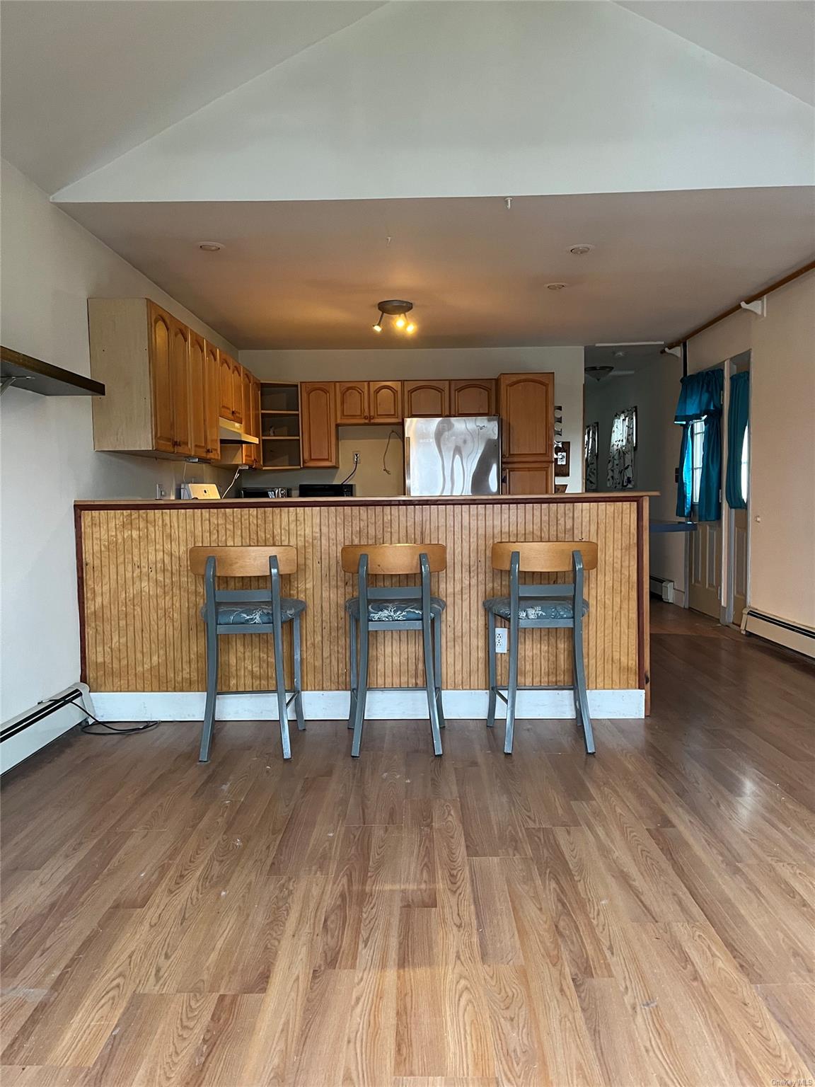 Kitchen with stainless steel refrigerator, kitchen peninsula, light hardwood / wood-style flooring, and a breakfast bar area