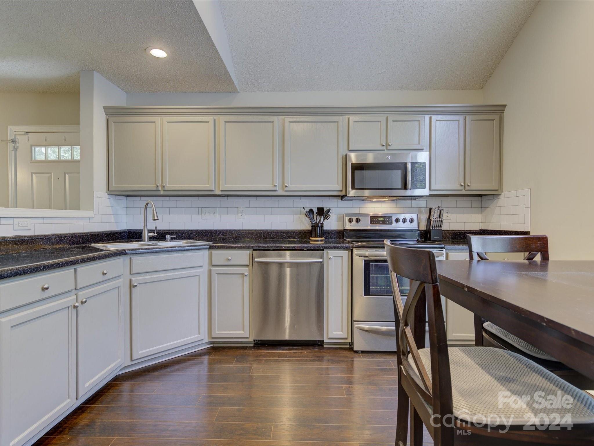 a kitchen with stainless steel appliances granite countertop a stove a sink a microwave a window and white cabinets